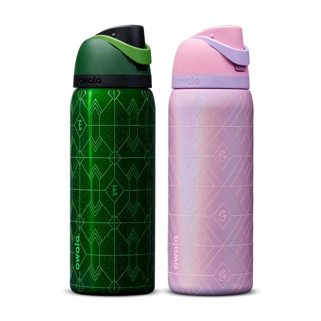 Owala Wicked 32oz FreeSip bundle showing two bottles side by side — deep emerald green Elphaba edition with geometric diamond-pattern texture and dark green flip cap, and shimmery iridescent lavender-pink Glinda edition with pink flip cap